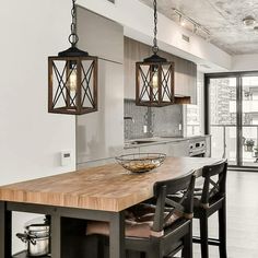 a kitchen with two pendant lights hanging from the ceiling over a wooden table and chairs