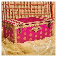 a pink and gold trunk sitting on top of a bed