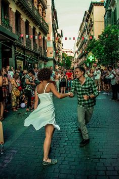 a man and woman dancing in the middle of a street with lots of people watching