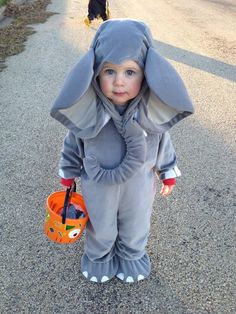 a little boy dressed up as a rabbit with a pumpkin in his hand and another person walking behind him