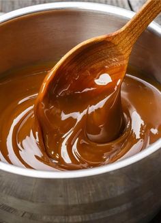 a wooden spoon in a metal bowl filled with melted caramel and brown liquid,