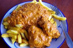 a blue plate topped with french fries and meat covered in gravy on top of a wooden table