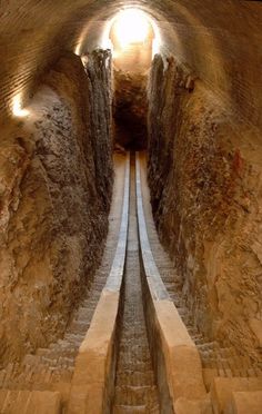 a narrow tunnel with stairs leading up to the top and down into the ground, in which there is only one light at the end