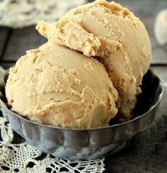 two scoops of ice cream sit in a metal bowl on a lace doily