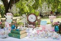 a table topped with lots of different types of cakes and cupcakes next to a clock