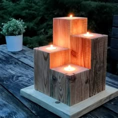 three wooden blocks with lit candles in them on a table next to some plants and trees