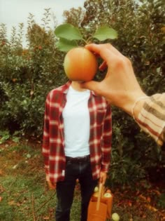 a person holding an orange in front of their face with one hand and the other on his shoulder