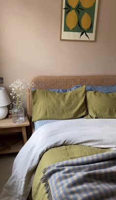 a bed with green and blue comforter next to a painting hanging on the wall