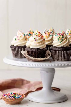 chocolate cupcakes with white frosting and sprinkles on a cake plate