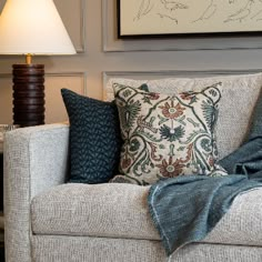 a living room with a couch, lamp and pictures on the wall above it that are also displaying artwork