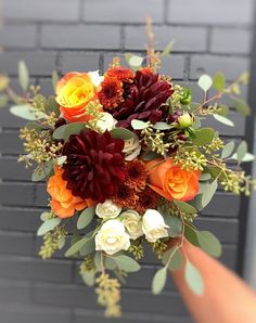 a person holding a bouquet of flowers in front of a brick wall with greenery