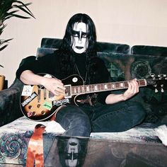 a man sitting on top of a couch with a guitar in his hand and face painted