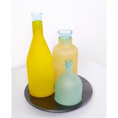 three different colored glass bottles sitting on a metal plate with a white wall in the background