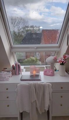 a room with a large window and a white desk in front of the window is a pink candle