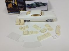 a white toy car next to it's box and its contents on a table