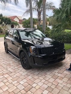 a black suv parked in front of a palm tree on a brick driveway next to a man