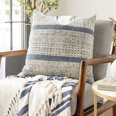 a chair with a blanket on top of it next to a table and potted plant