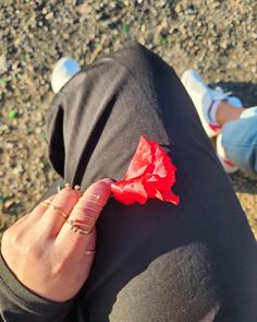 a person holding a red flower in their left hand with both hands on the ground