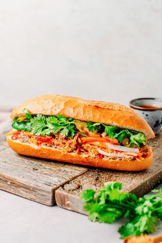 a sandwich with meat, lettuce and tomato on a cutting board next to some dipping sauce