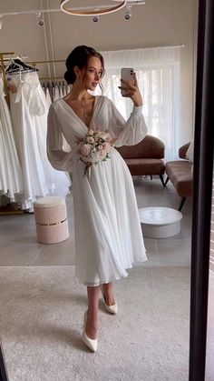 a woman taking a selfie in front of a mirror wearing a white wedding dress