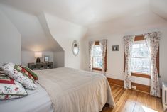 a bed sitting in a bedroom next to two windows on top of a hard wood floor