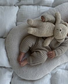 a baby is laying down on a bed with a stuffed animal in it's arms