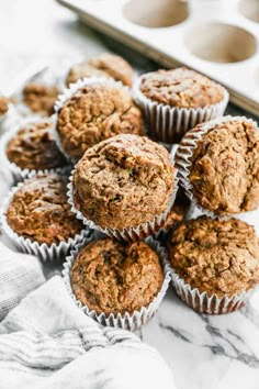 muffins stacked on top of each other in front of a baking tray with more muffins nearby