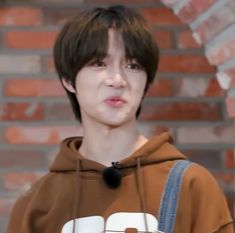 a young man wearing a brown hoodie standing in front of a brick wall