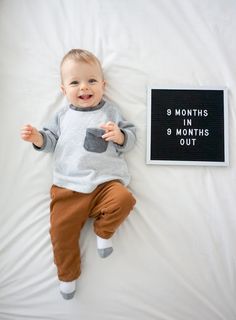 a baby laying on top of a bed next to a sign that says 9 months 3 months out