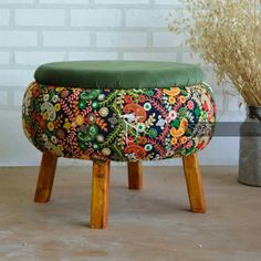 a small stool with a green cushion on it next to a potted plant and brick wall