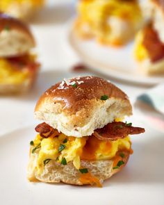 an egg, bacon and cheese breakfast sandwich on a biscuit roll with two plates in the background