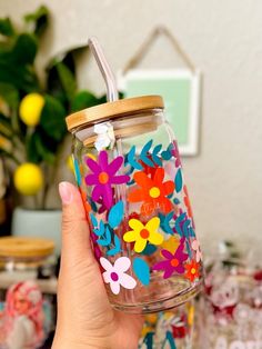 a person holding a glass jar with flowers on it and a straw in the bottom