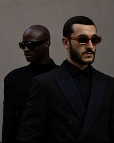 two men in black suits and sunglasses standing next to each other with one man's face partially obscured by the sun glasses