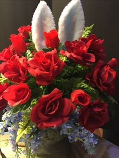 a vase filled with red roses and white bunny ears