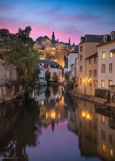 a river running through a city with buildings on the hillside in the background at dusk