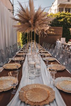 a long table is set with gold plates and place settings for an outdoor dinner party