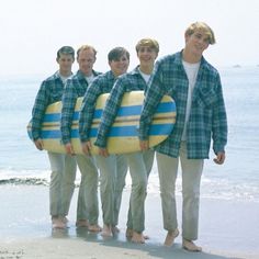 four young men are holding surfboards on the beach