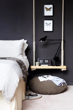 a bedroom with black walls, white bedding and a wooden swing hanging from the ceiling