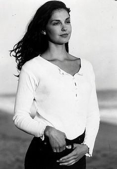 a black and white photo of a woman standing on the beach with her hands in her pockets