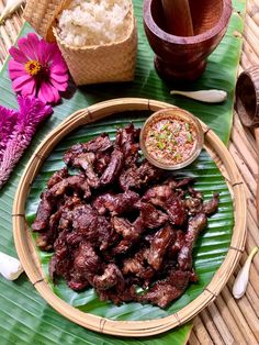 a plate full of meat and rice on a table with some purple flowers in the background