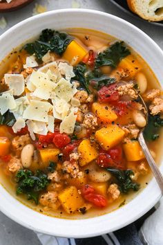 a white bowl filled with meat and vegetable soup on top of a blue towel next to bread