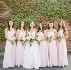 a group of women standing next to each other in front of a brick wall holding bouquets