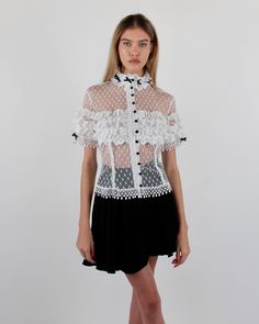 Introducing the elegant Alicia Blouse, crafted from Swiss Point D’Esprit with cotton lace ruffles, Venise trims, and satin baby bows. This soft, fitted blouse features an empire focus, adorned with delicate ruffles at the neckline and sleeves, complemented by satin pearl buttons at the center front. Available in White and Black or Black on Black. Swiss Point D’Esprit Cotton lace ruffles with Venise trims Satin pearl buttons Dry clean only Each piece is made to order and handcrafted in our atelie Designer Ruffled Summer Tops, White Fitted Lace Top With Contrast Lace, Designer Ruffled Tops For Summer, Fitted White Lace Top With Contrast Lace, Short Sleeve Lace Top With Ruffles, Elegant Spring Lace Top With Contrast Lace, Elegant Summer Lace Top With Lace Cuffs, Designer Ruffled Tops For Evening, Designer Ruffle Tops For Evening