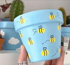 a hand holding up a blue flower pot with bees on it