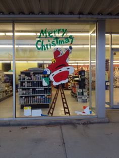 a store front with a christmas sign in the window and santa clause on it's ladder