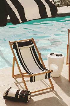 A poolside setting featuring black-and-white striped deck chairs and a matching rolled beach towel, paired with a white modern side table holding sunglasses. The sparkling pool water and relaxed vibe exude effortless sophistication. Sling Chair, Vintage Elegance, Garden Set, Resort Collection, Outdoor Brands, Beach Pool, Scalloped Edge, Outdoor Seating