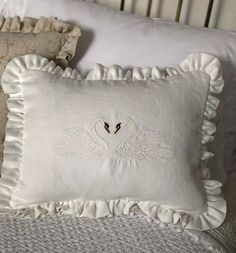 two white pillows on a bed with ruffled edges and an embroidered swan applique