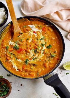 a pan filled with curry and rice next to a wooden spoon