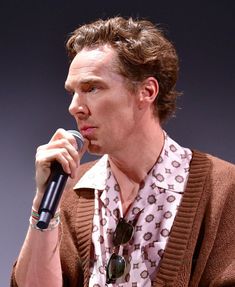 a man holding a microphone up to his mouth while wearing a sweater and bracelets