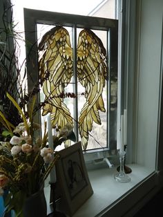 two stained glass angel wings sitting on a window sill next to a vase with flowers